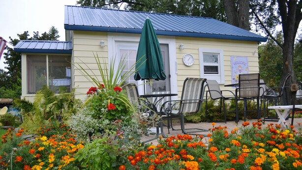 A yellow building with a blue roof, a green umbrella, and outdoor seating. - LYC Cottage #1 (Port Austin)