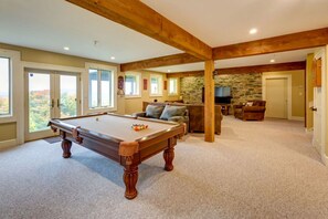 Une table de billard dans une pièce spacieuse, avec un mur en pierre, un canapé et un téléviseur.