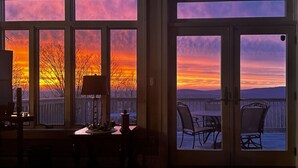 A room with a view of a sunset through large windows, a dining table, and chairs. - Luxury Mountaintop Estate – Spacious Retreat with Breathtaking Views (Bovina Center)