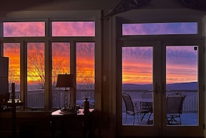 A room with a view of a sunset through large windows, a dining table, and chairs.