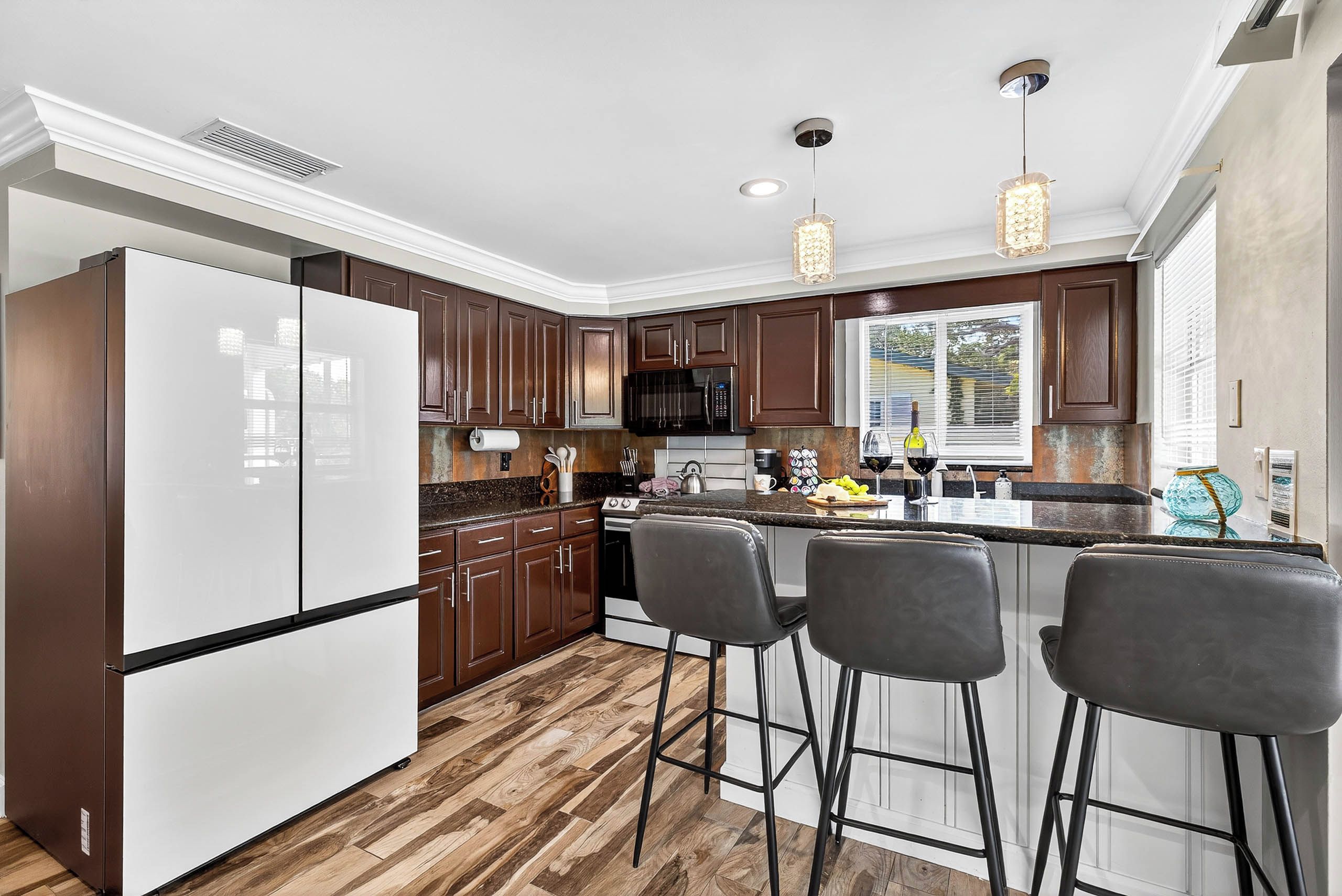 A modern kitchen with a refrigerator, dark wooden cabinets, a stainless steel range, and a bar area with stools.