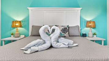 A bed with a white headboard, two nightstands with lamps, and a pair of towels arranged in a heart shape.