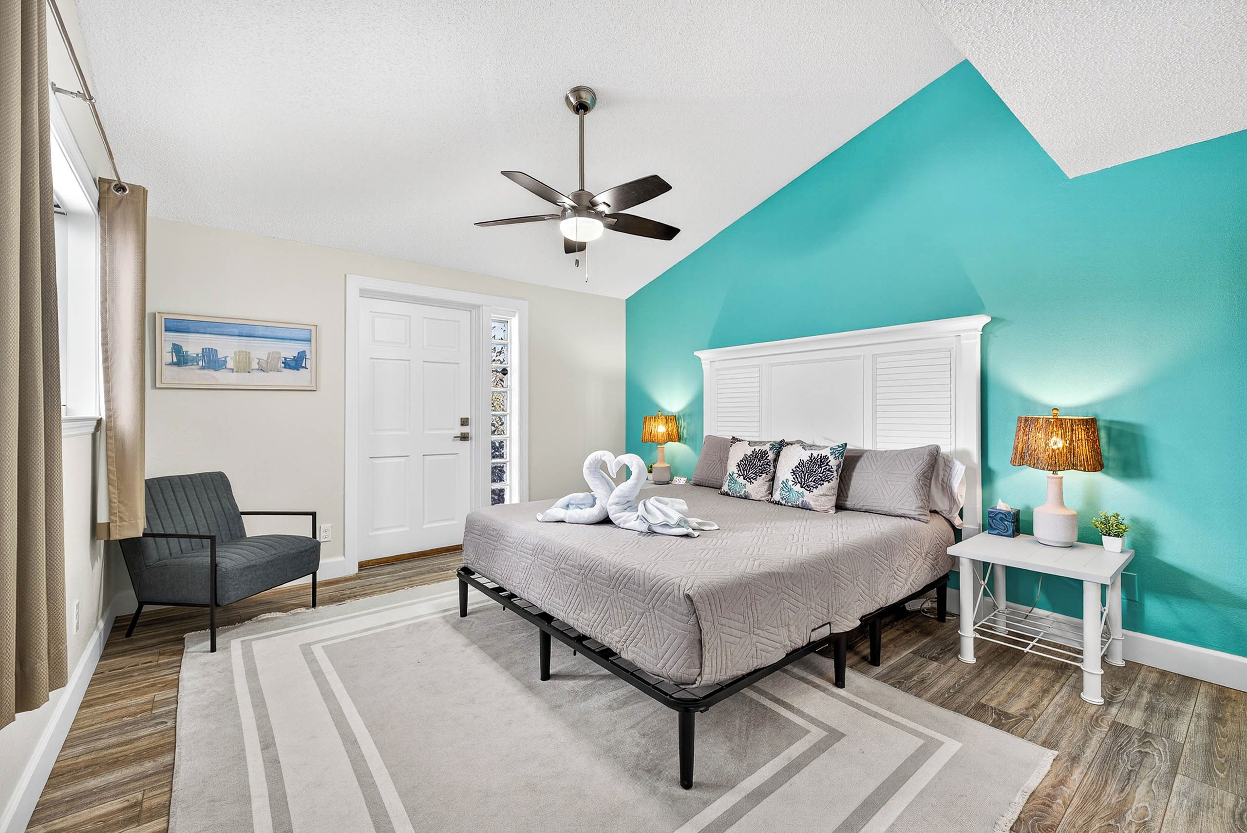 A bedroom with a bed, a chair, a ceiling fan, and a door.
