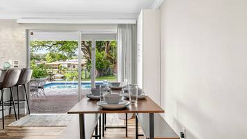 A dining area with a table set for four, a pool visible through the glass door, and a view of a residential area outside.