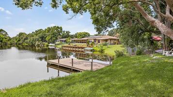 A lakeside property with a dock, a house with a covered patio, and lush greenery.