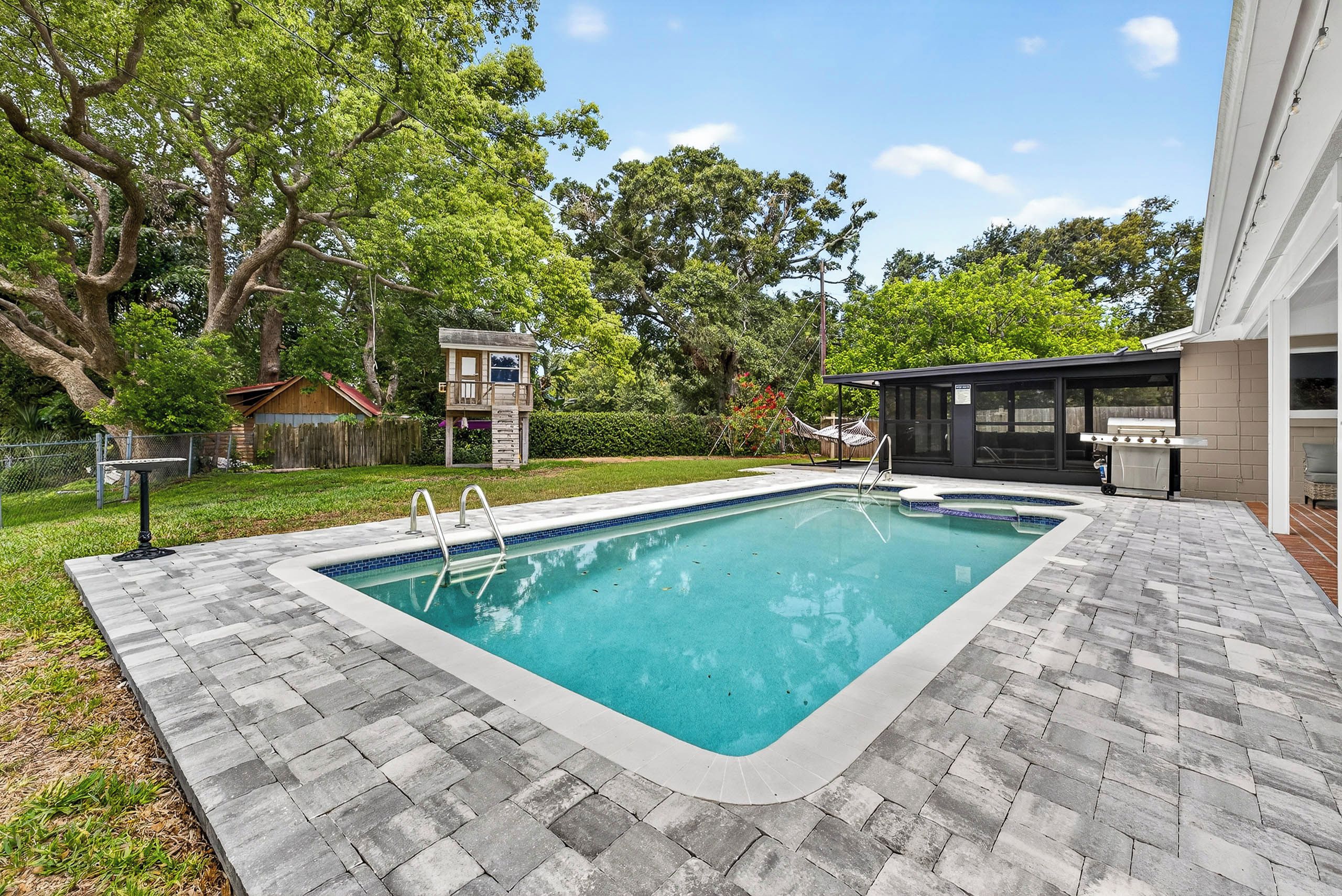 A rectangular swimming pool with a tiled edge, surrounded by a brick patio.