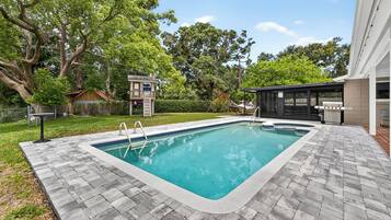 A rectangular swimming pool with a tiled edge, surrounded by a brick patio.