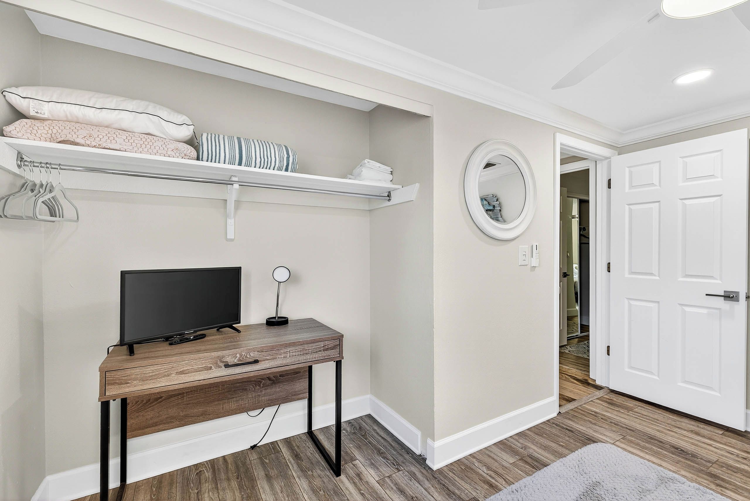A room with a wooden desk, a television, a mirror, and a white door.
