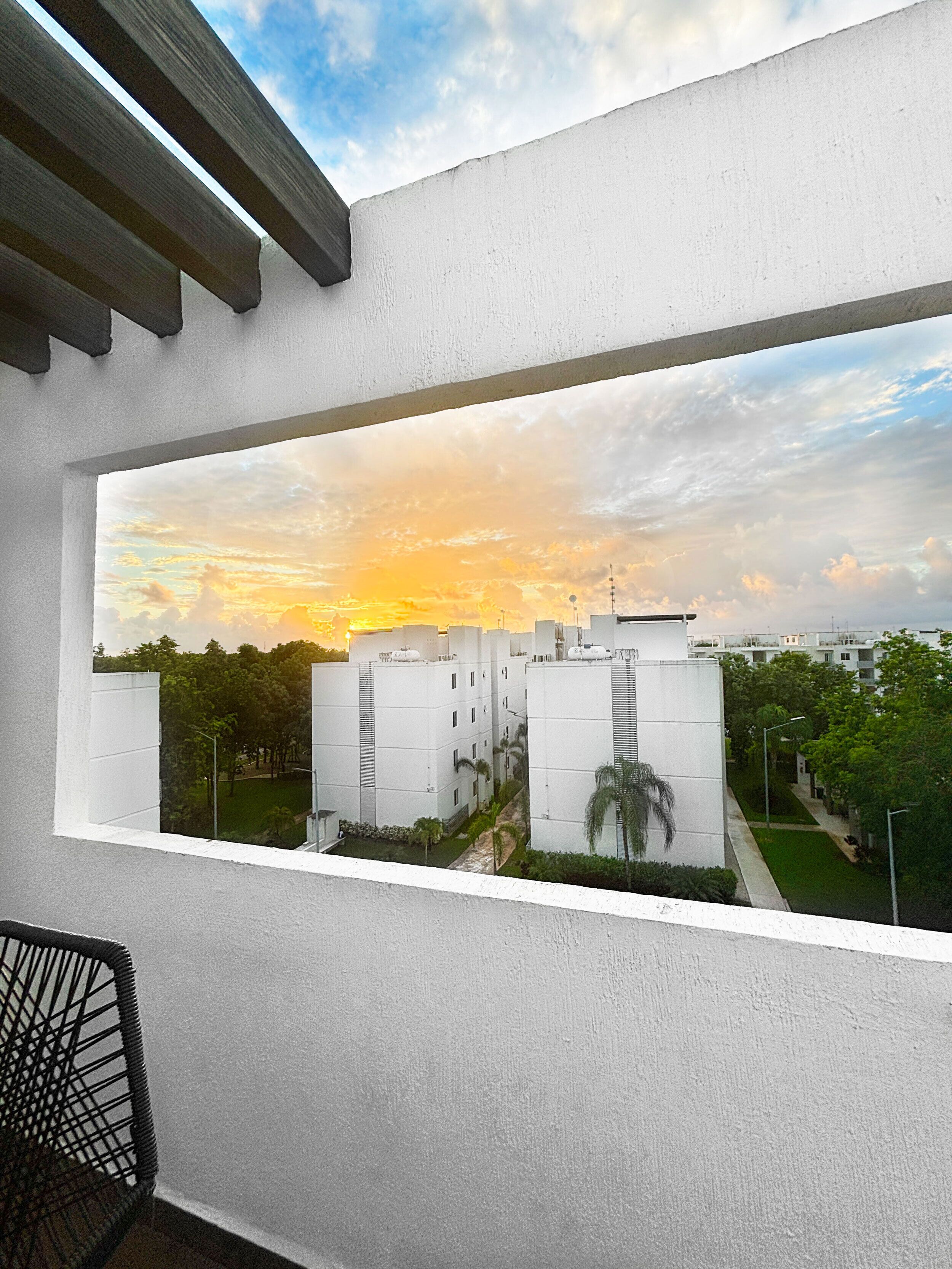 A view through a window of a building complex with multiple white structures, a clear sky, and some greenery.