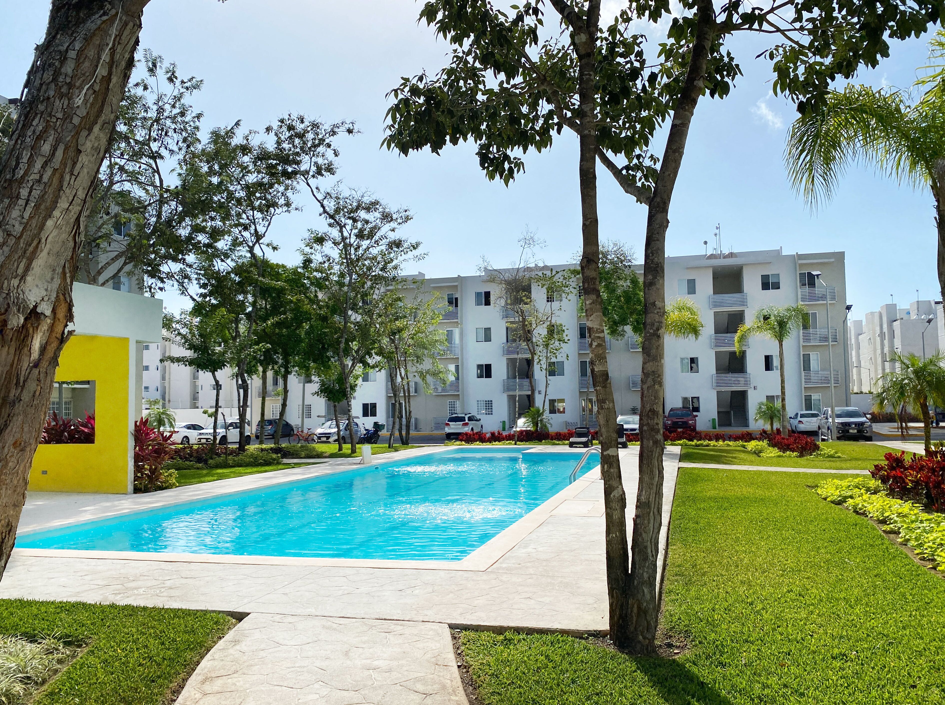 A swimming pool surrounded by grass and trees, with a modern building in the background.