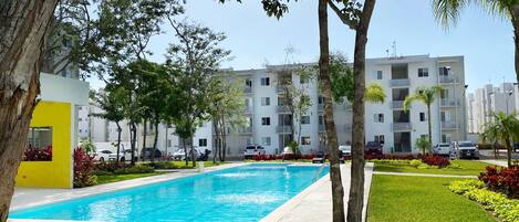 A swimming pool surrounded by grass and trees, with a modern building in the background.