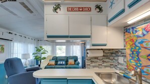 Un espacio habitable pequeño con kitchenette, un sofá con cojines, un sillón azul y un mural de pared colorido.