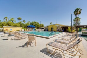 A pool area with lounge chairs and umbrellas, surrounded by palm trees and a building with a yellow facade. - Resort Pool & Sports Courts! Port Charlotte Home (Port Charlotte)