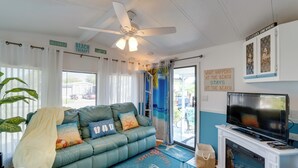 Una sala de estar acogedora con un sofá verde azulado, un ventilador de techo, un televisor y una chimenea.
