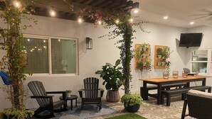 A patio area with a wooden table and chairs, a small rug, and potted plants.