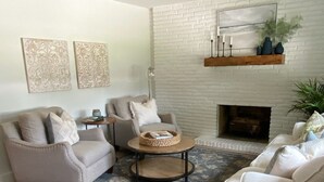 A living room with a white brick fireplace, two armchairs, a coffee table, and a patterned rug.