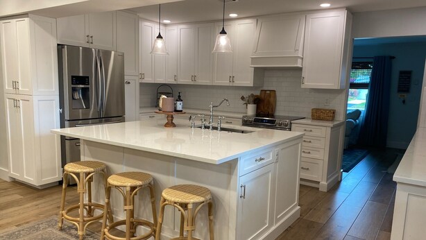 A modern kitchen with white cabinetry, a large island with stools, stainless steel appliances, pendant lighting, and a view to the outside.