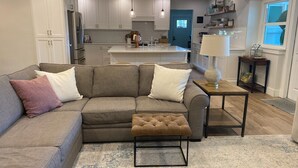 A modern living room with a grey sofa, a brown ottoman, and a patterned rug.