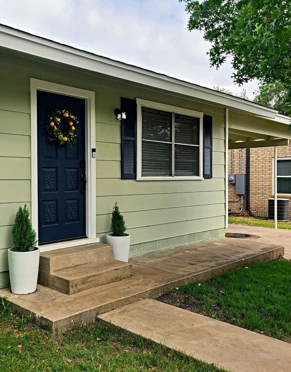 A house with a dark blue front door, a wreath, and two potted plants.