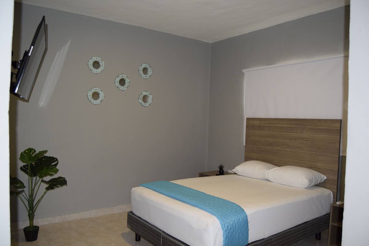 A bedroom with a bed, a TV mounted on the wall, and a potted plant.