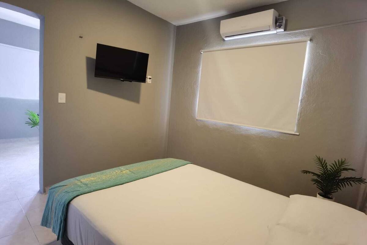 A bedroom with a bed, a television mounted on the wall, and an air conditioning unit.