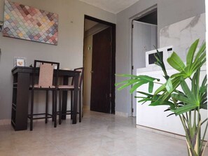 A room with a dining area featuring a table and chairs, a large potted plant, and a white wall with a marble-like texture.