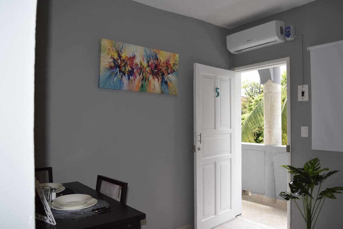 A dining area with a table set for two, a painting on the wall, and a door leading outside.