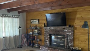 A cozy living room with a fireplace, a television mounted above it, and a bookshelf filled with books and decorative items.