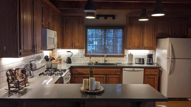 A kitchen with wooden cabinets, a gas stove, a microwave, a sink, and a refrigerator.