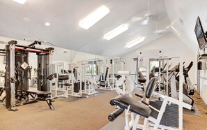 Une salle de sport équipée de divers appareils d’exercice, dotée d’un mur avec des miroirs et d’un plafond avec des luminaires encastrés.
