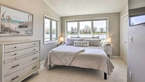 A bedroom with a large bed, a dresser, two bedside tables, and a window with a view of the outdoors. - Lakefront Bellevue Home: Private Beach & Fire Pit! (Bellevue)
