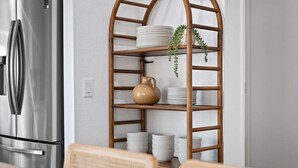 A kitchen with a stainless steel refrigerator, a wooden shelf unit with plates and bowls, and a hanging plant. - Golfer`s Delight | Pool Club House + BBQ Island (Indio)