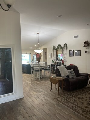 A spacious living room with a brown leather sofa, a dining area with a white table and chairs, and a kitchen in the background. - Country Living in the City 3400 sq. ft. (Peoria)