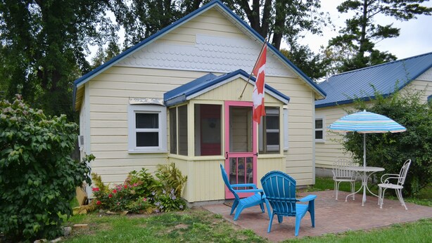 Ein Haus mit einer Veranda, zwei blauen Stühlen, einem Tisch und einem gestreiften Sonnenschirm.