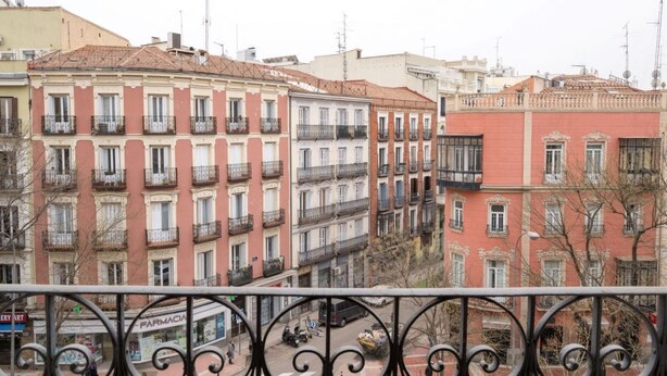 A row of multi-story buildings with balconies, a pharmacy, and a visible street with parked vehicles. - Apartamento Premium 2 Dormitorios 1 Baño con Balcón (Madrid)