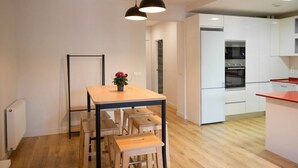 A modern kitchen with white cabinets, a wooden dining table, and black pendant lights. - Apartamento Premium 2 Dormitorios 1 Baño con Balcón (Madrid)