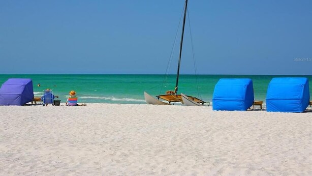A beach with a sailboat, covered chairs, and a tent.