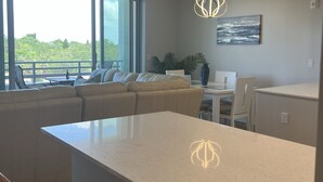 A modern kitchen with a large island, pendant lighting, and a view of greenery outside.