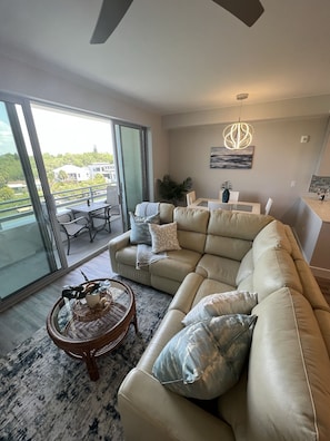 Een moderne woonkamer met een beige modulaire bank, een ronde salontafel en uitzicht op een balkon met een eethoek.