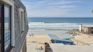 A beachfront property with a 'For Rent' sign, a beach view, and a building with a blue roof. - Top Floor Panoramic Whitewater Ocean Views in Oceanside! 1,081 Sq Ft (Oceanside)