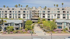 A multi-story hotel with balconies, a central courtyard, and palm trees. - Top Floor Panoramic Whitewater Ocean Views in Oceanside! 1,081 Sq Ft (Oceanside)