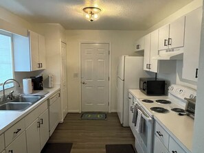 Compact kitchen with white cabinetry, stainless steel sink, microwave, refrigerator, and stove with four burners.