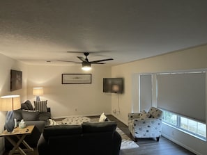 A living room with a ceiling fan, a TV mounted on the wall, a sofa, a coffee table, and a window with blinds.