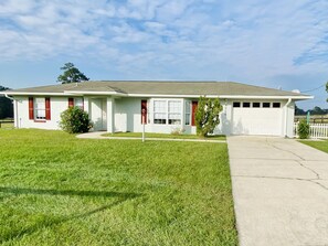 Stylish single-story home with a charming entrance, complete with a red door and shutters, set amidst a well-manicured yard.