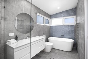 A modern bathroom with a freestanding bathtub, a double vanity with a mirror, and a window above the sink. - Bluehaven Woolgoolga (Woolgoolga)