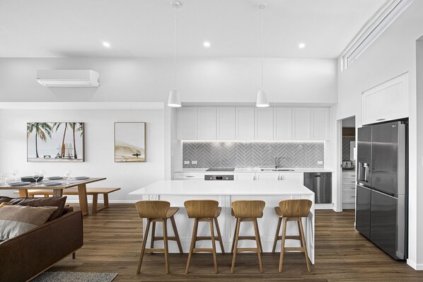 A modern kitchen with white cabinetry, a central island with bar stools, a stainless steel refrigerator, and a herringbone backsplash.