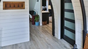 Ein Innenraum mit Holzwandverkleidung, einer hängenden Leuchte, einem Holzanziehkleiderständer und einer Tür mit beschlagenen Glasscheiben.