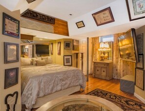 Cozy retreat with a large bed, dresser, and nightstand, surrounded by framed artwork and a patterned rug.