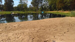 A sandy beach with footprints leading into a calm lake surrounded by trees. - Primitive campsites, pond, wildlife, campfires (West Frankfort)