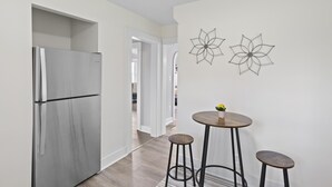 A modern kitchen with a stainless steel refrigerator, a round wooden table with stools, and two wall-mounted abstract art pieces. - Family and dog friendly☆3BR house☆Porch swing☆Mars☆PGH☆Cranberry (Mars)